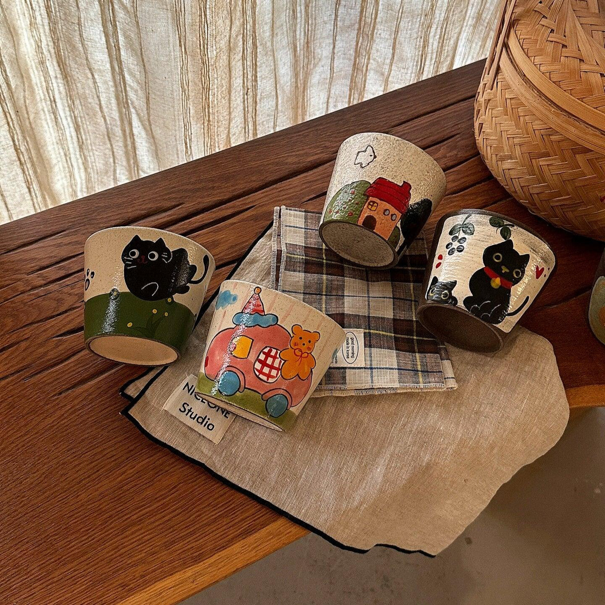 Hand-painted ceramic mugs with cute cat and house designs on wooden table