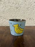 Handmade ceramic mug with cute yellow banana design, stars, light blue speckled glaze, perfect for coffee or tea