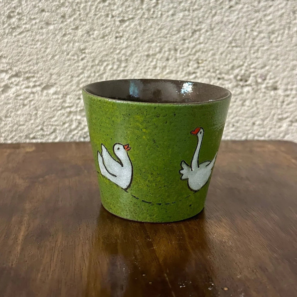 Green ceramic mug with white swan designs, handmade and food-safe, perfect for tea or coffee.