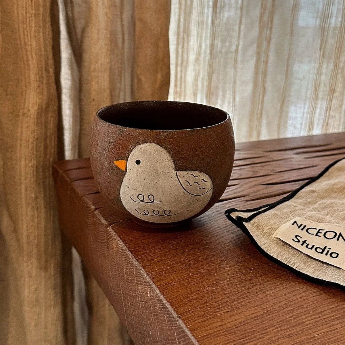 Handmade ceramic mug with cute bird design, perfect for coffee or tea, displayed on wooden table