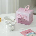 White ceramic mug with silver bow handle beside pink gift box, perfect for tea or coffee