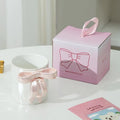 White ceramic mug with pink bow handle beside gift box, ideal for tea or coffee lovers