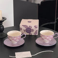 Purple floral ceramic tea cups with matching saucers, gift box, and pearl necklace on black table