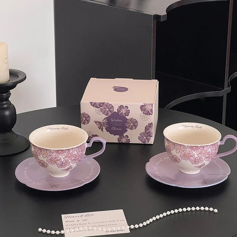 Purple floral ceramic tea cups with matching saucers, gift box, and pearl necklace on black table