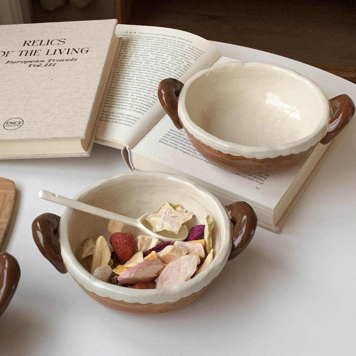 Handmade ceramic bowls with dried fruit, styled beside an open book for cozy tea moments.