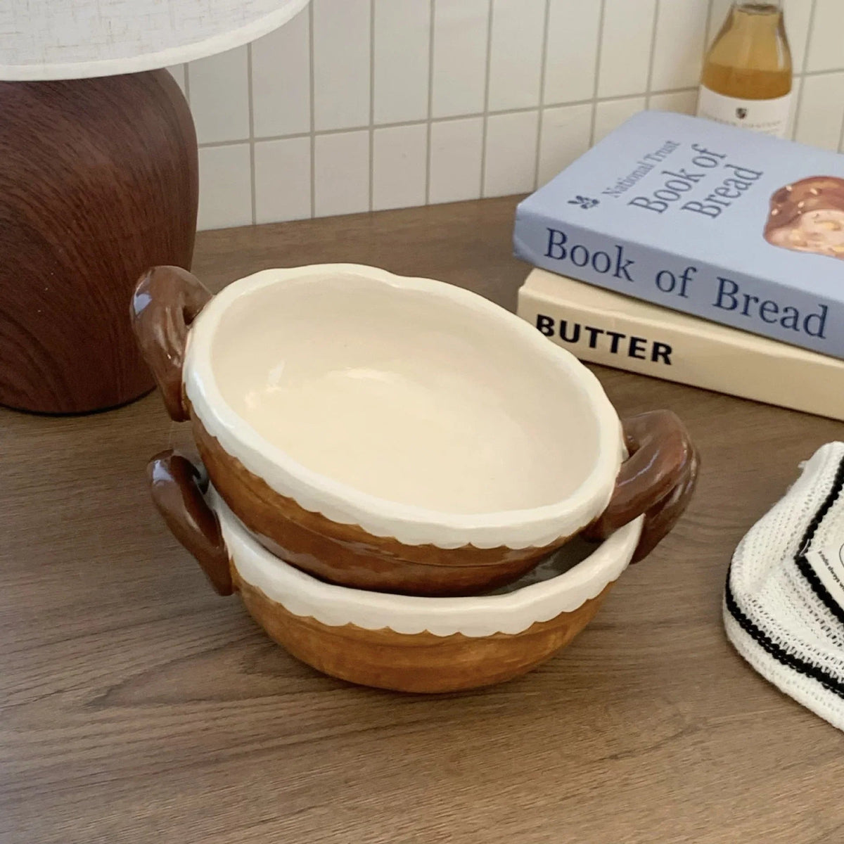 Handmade ceramic bowls with scalloped edges and handles, styled on wood table with cookbooks